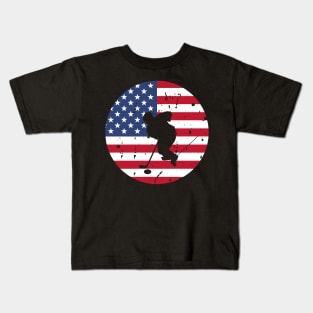 American Flag and Ice Hockey Player Silhouette, A silhouette of an ice hockey player overlaid on a distressed American flag, encapsulating patriotism and sportsmanship. Kids T-Shirt